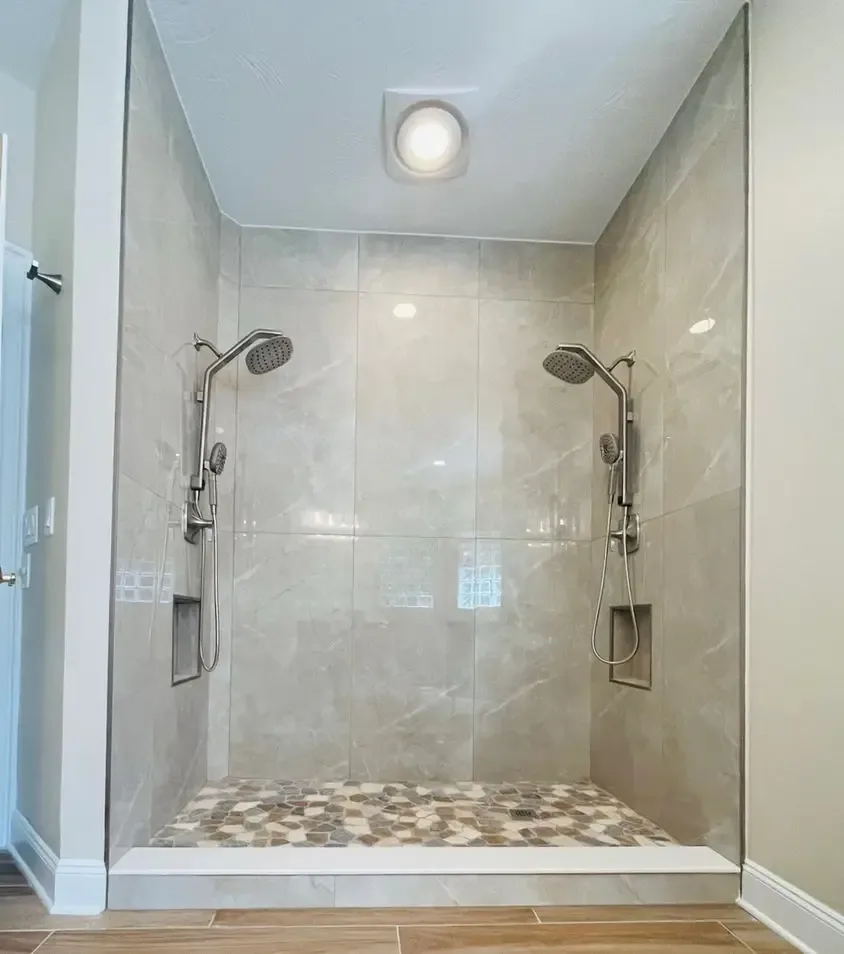 A tiled walk-in shower with twin shower heads and a pebble-tile floor