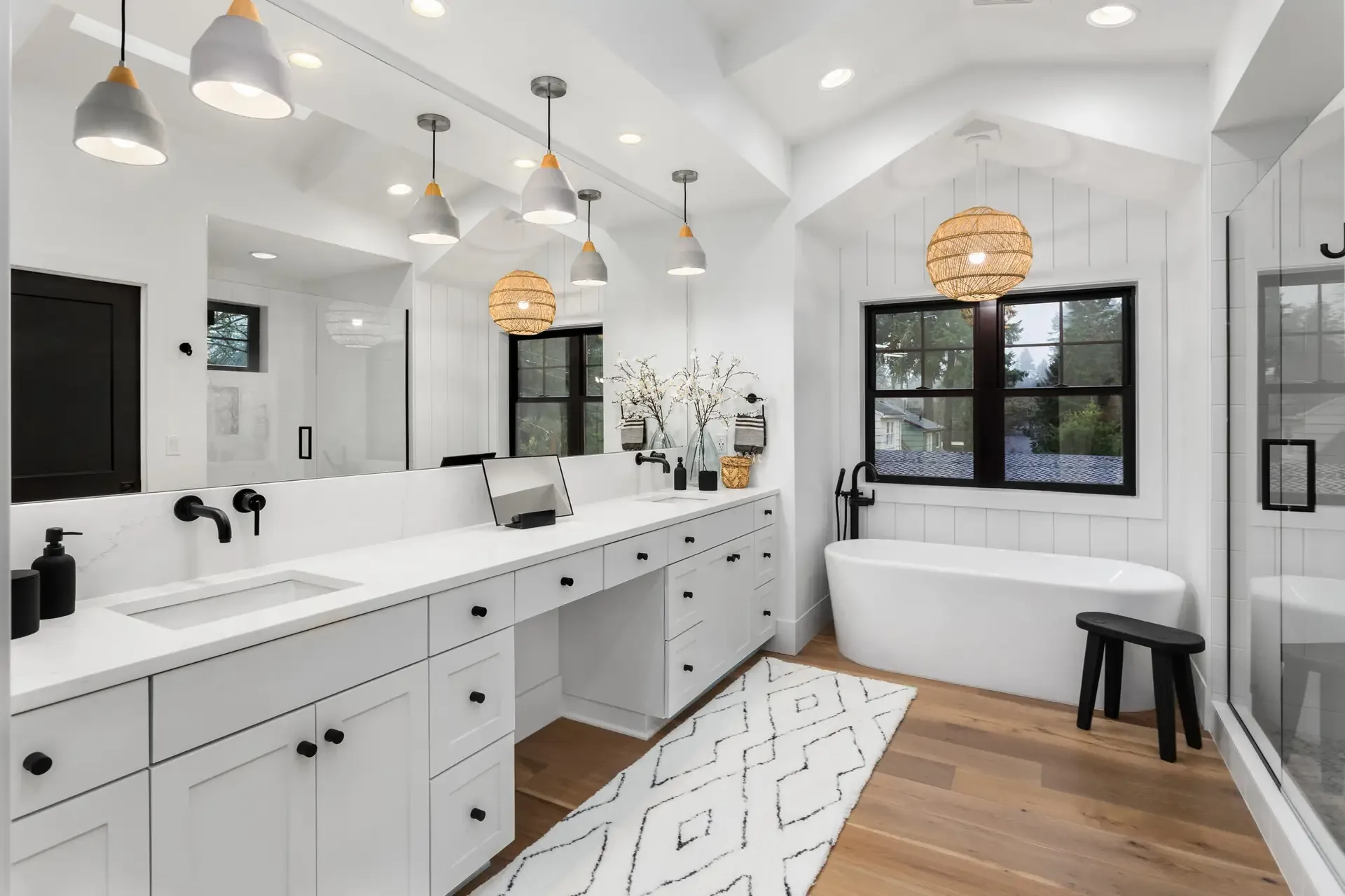 A master bathroom with a long double vanity, freestanding tub and black-framed windows