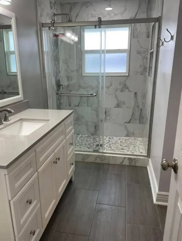 A bathroom with a white vanity, marble-look tiled shower and wood-look floor tile