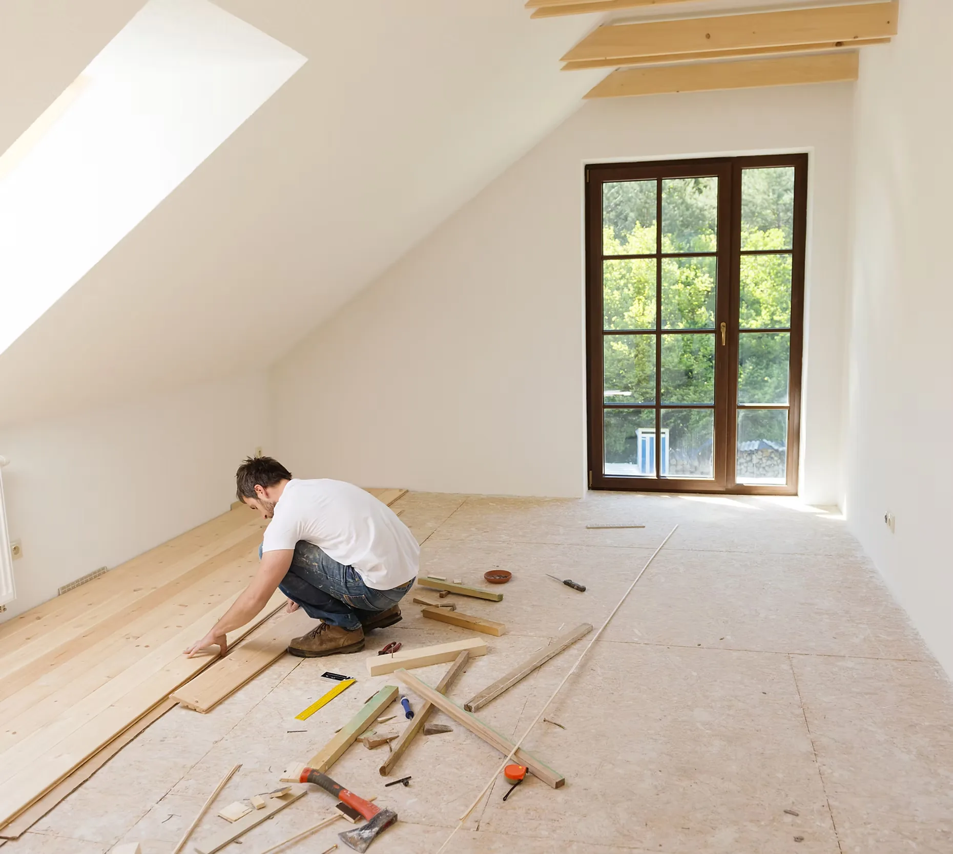 A flooring installer laying wood plank flooring in a bright empty room