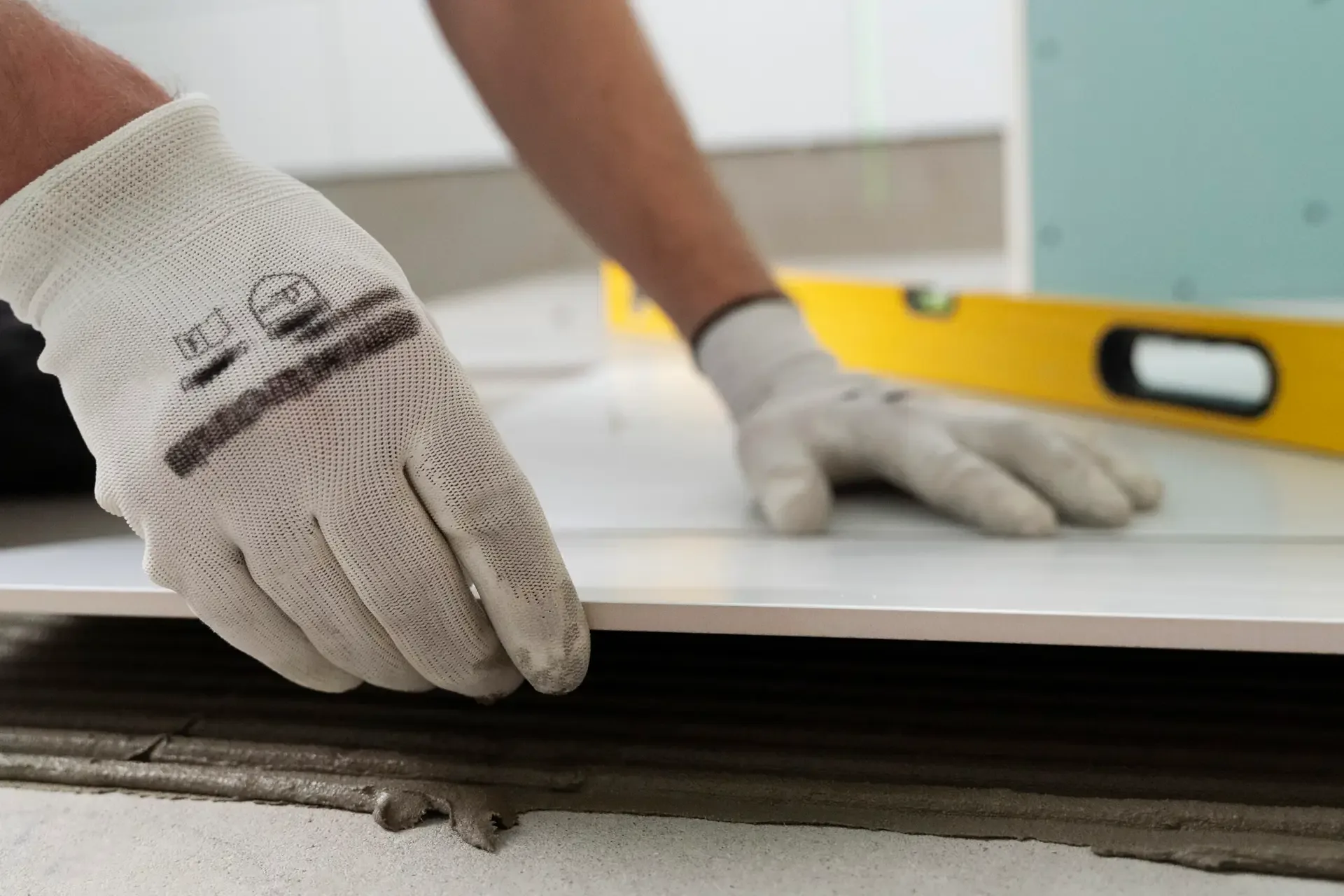 A gloved tiler bedding a large floor tile into fresh adhesive