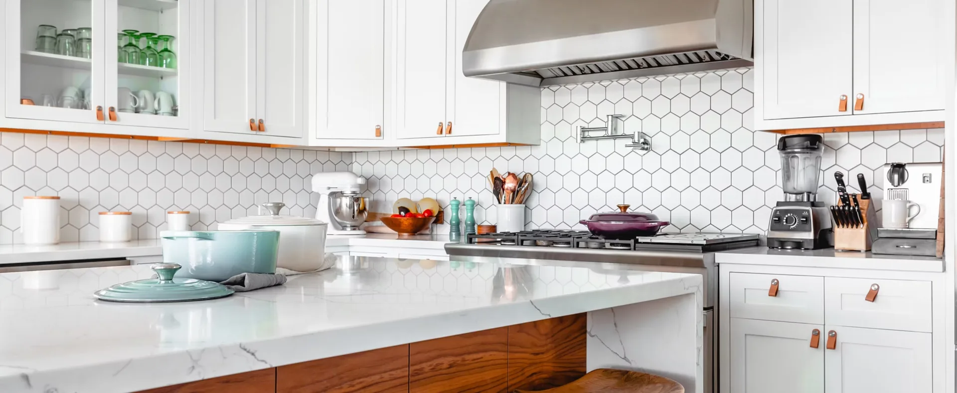 A white kitchen with a hexagonal tile backsplash, walnut counter and stainless range