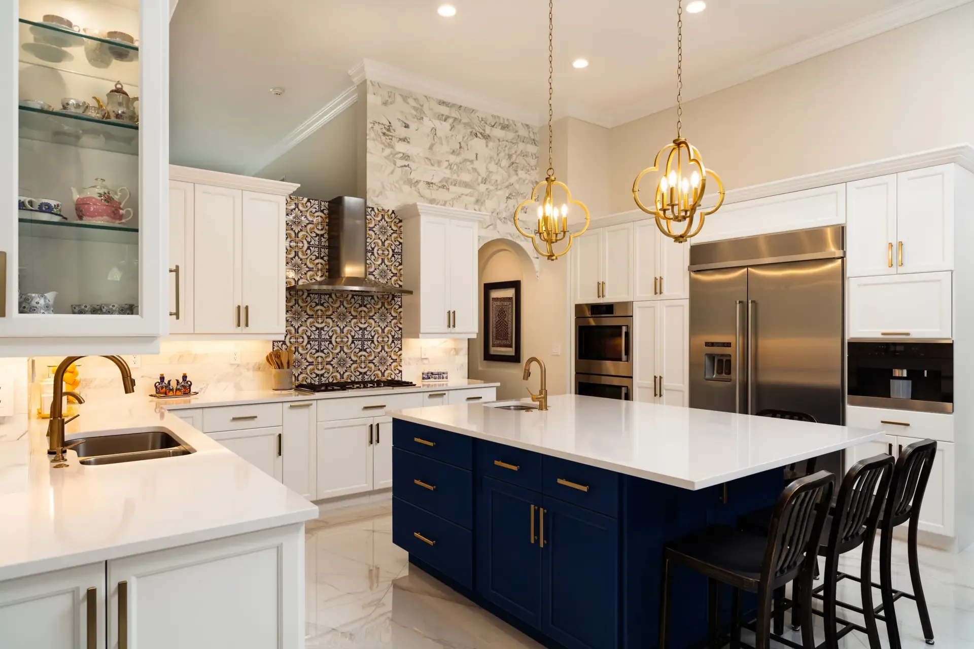 A white kitchen with a navy blue island, gold pendant lights and a patterned tile backsplash