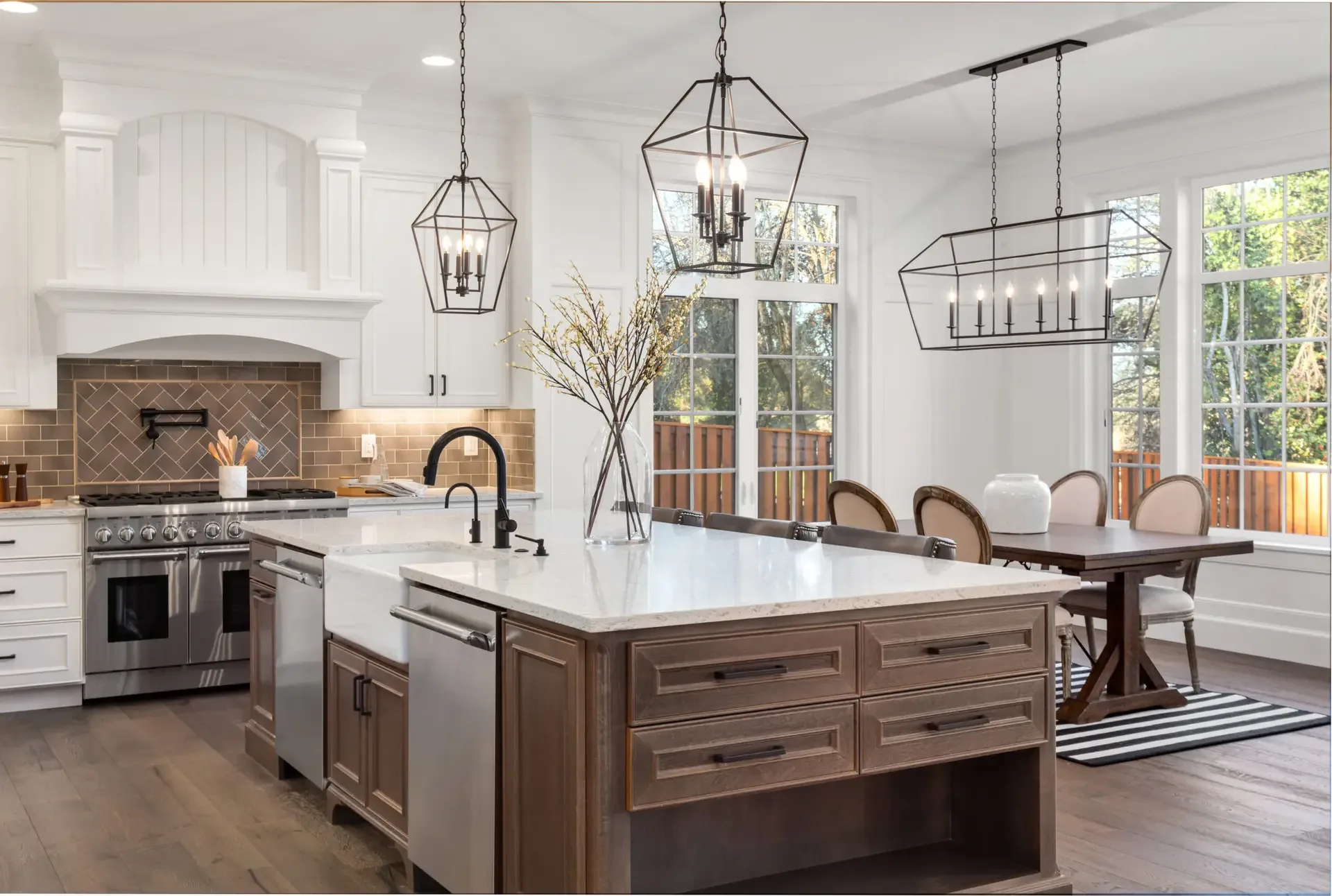 An open-plan white kitchen with a walnut island, lantern pendant lights and a dining area beyond
