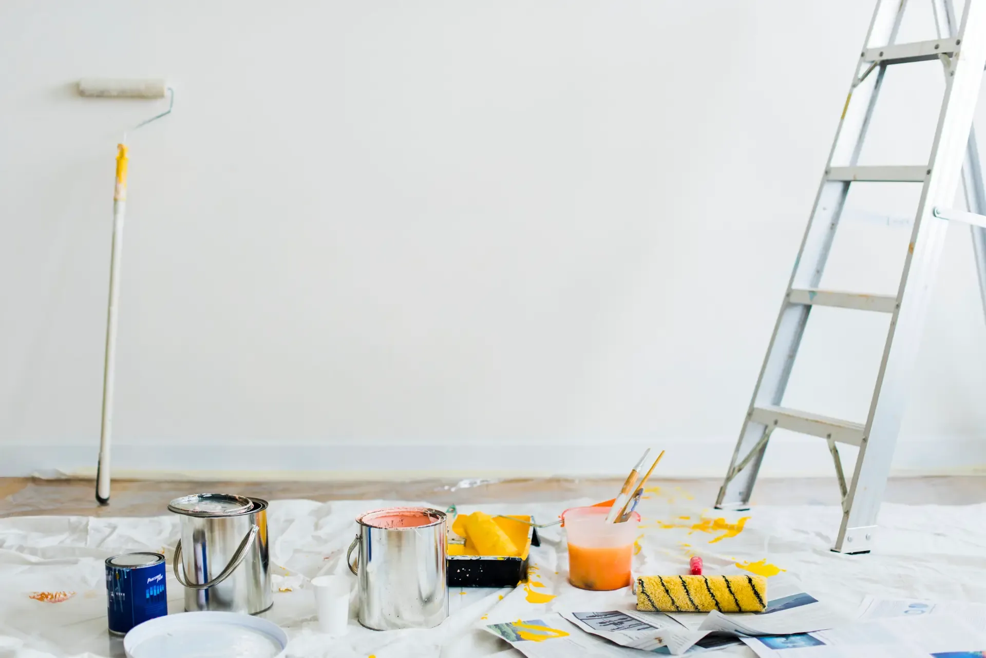 Paint buckets, a roller and a ladder on a drop cloth in a room being painted