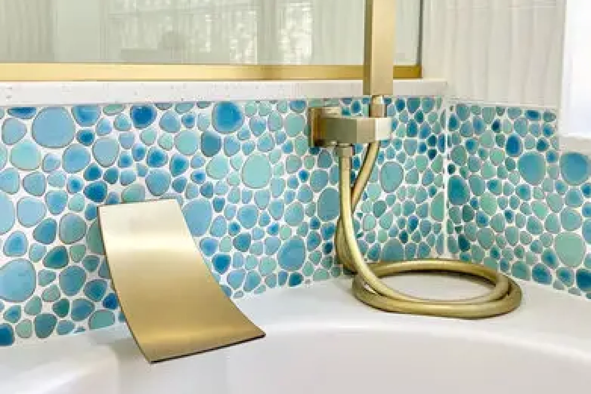 Close-up of aqua pebble tile and gold faucet fixtures in a custom bathtub remodel by GIL Renovation Services.