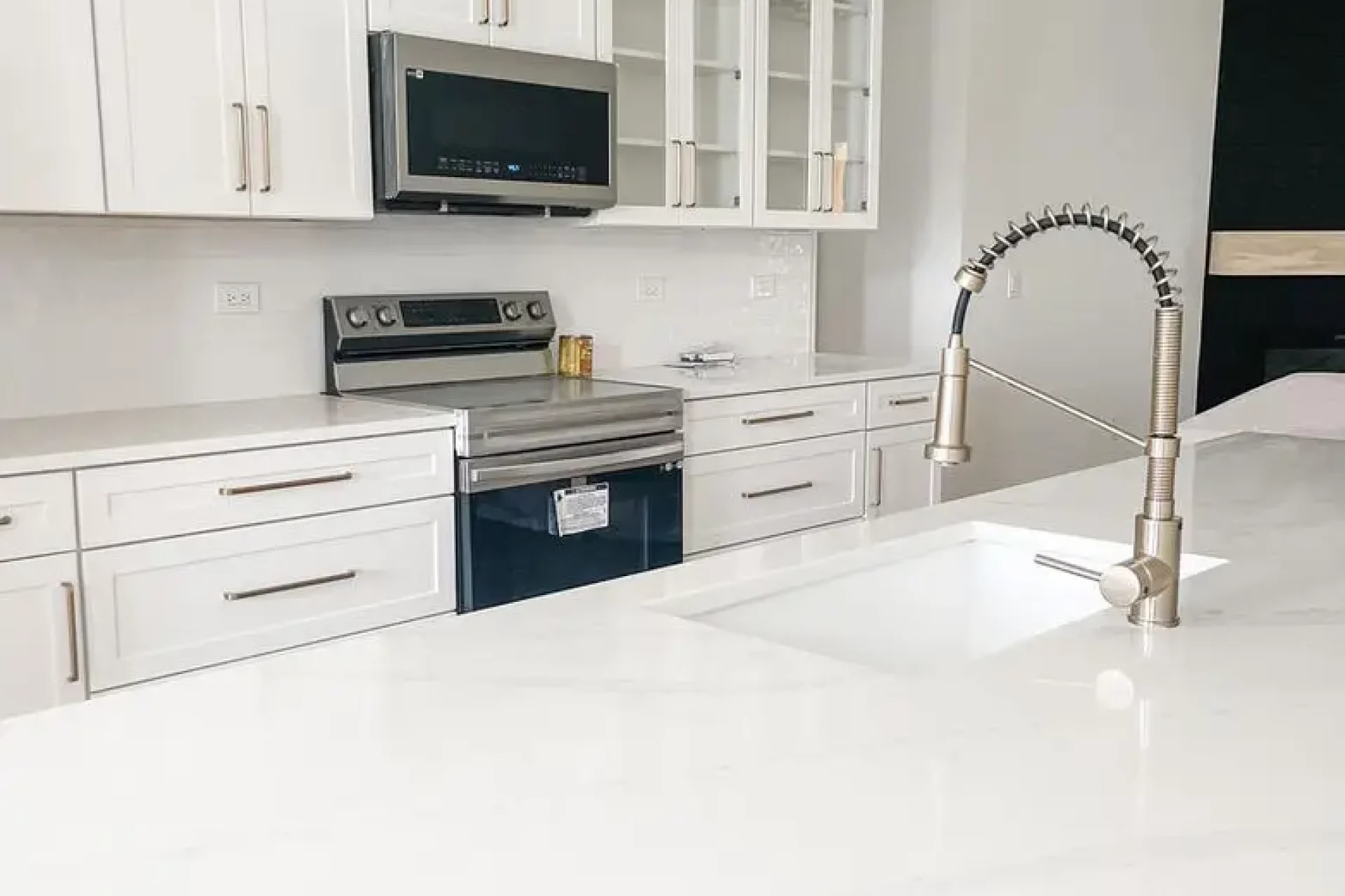 Bright white kitchen remodel with glass cabinet doors and modern stainless-steel faucet by GIL Renovation Services.