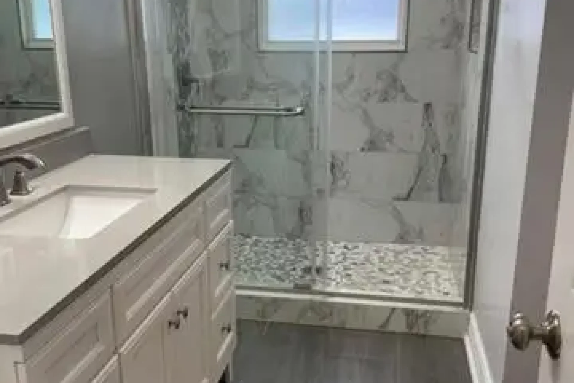 Small bathroom remodel with marble shower walls, sliding glass door, and dark tile flooring by GIL Renovation Services in Jacksonville.